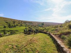 An outdoor grassy area with a rotary clothesline and a table with chairs surrounded by hills at Roger Pot in Garsdale near Sedbergh