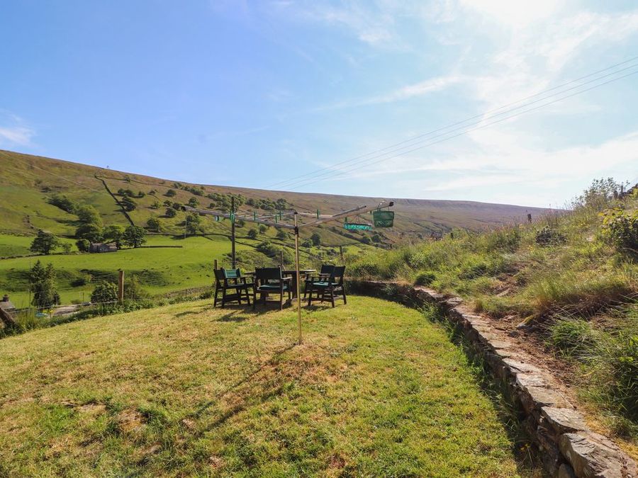 An outdoor grassy area with a rotary clothesline and a table with chairs surrounded by hills at Roger Pot in Garsdale near Sedbergh