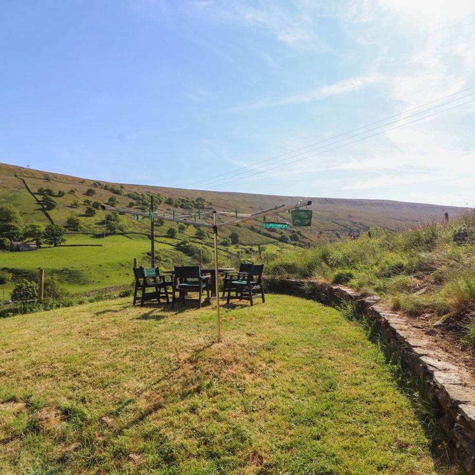 An outdoor grassy area with a rotary clothesline and a table with chairs surrounded by hills at Roger Pot in Garsdale near Sedbergh