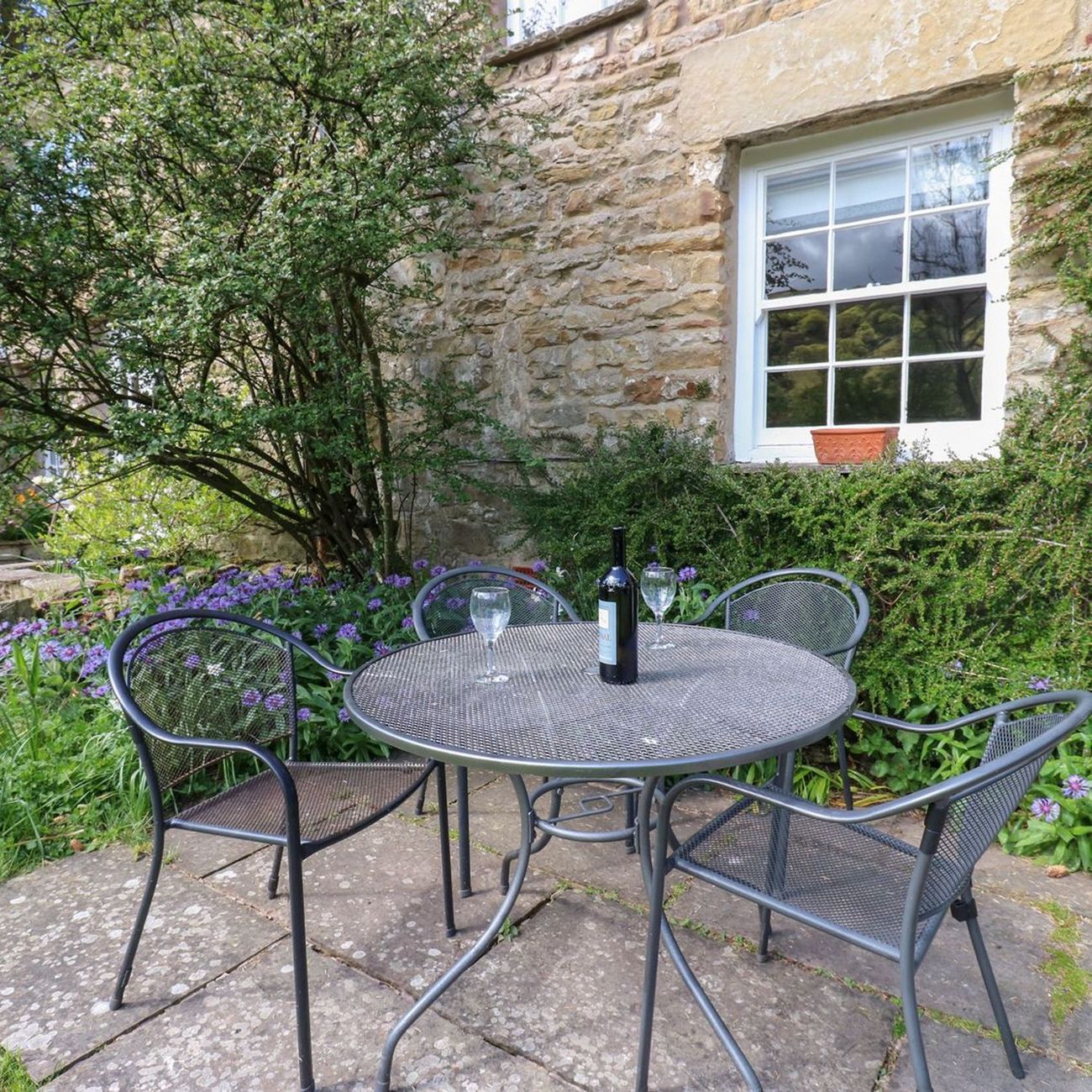A table and four chairs on the patio at Farrier's Cottage, sheltered by the cottage wall with flowers in the border