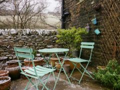 An outdoor patio with two mint green chairs and a round table near a stone wall with potted plants at The Old Cart House in Garsdale near Sedbergh
