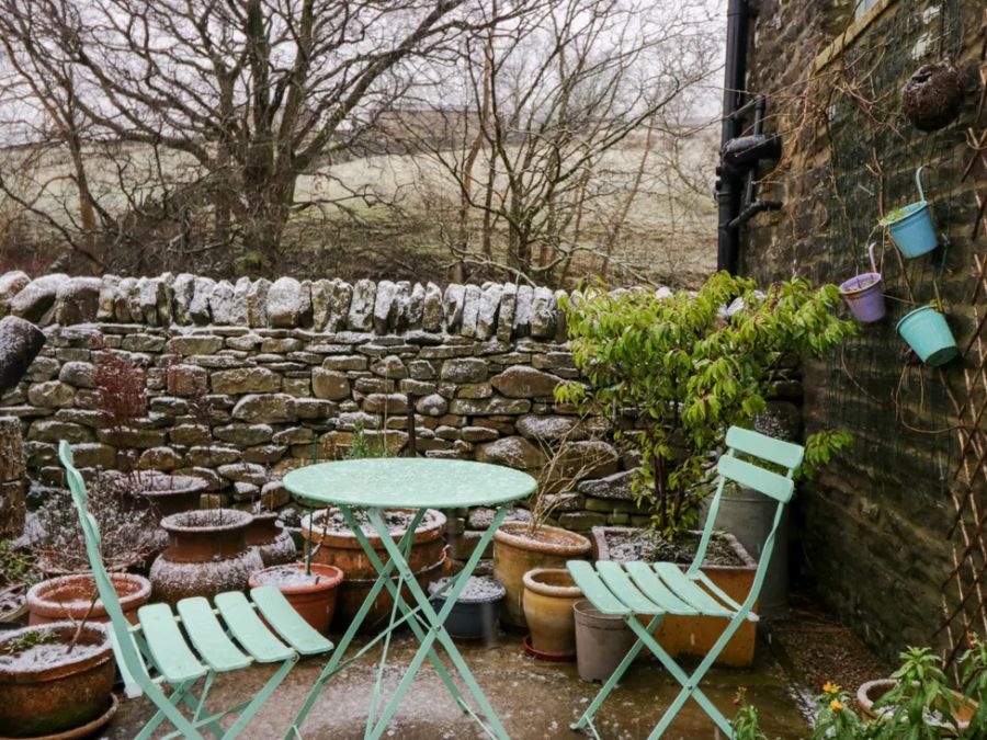 An outdoor stone patio with metal table and chairs surrounded by pots and a stone wall at The Old Cart House in Garsdale near Sedbergh