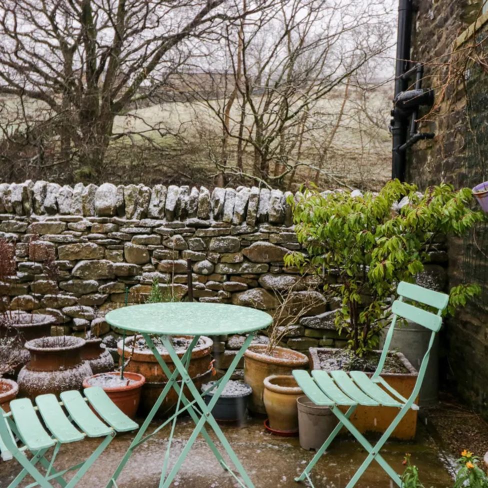 An outdoor stone patio with metal table and chairs surrounded by pots and a stone wall at The Old Cart House in Garsdale near Sedbergh
