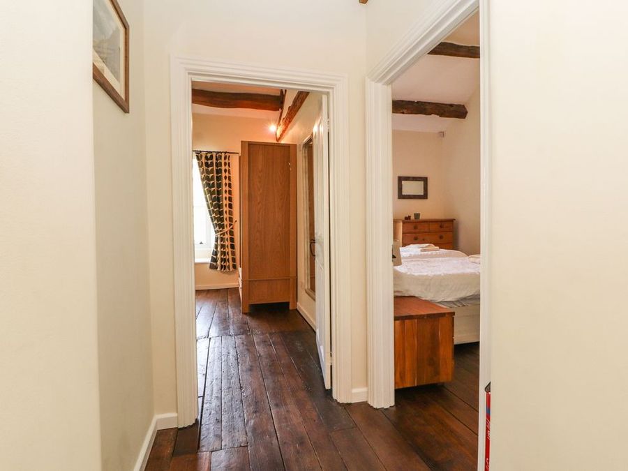 Hallway with wooden floor leading to a bedroom with bed and dresser and another room with wardrobe and window at Roger Pot in Garsdale near Sedbergh
