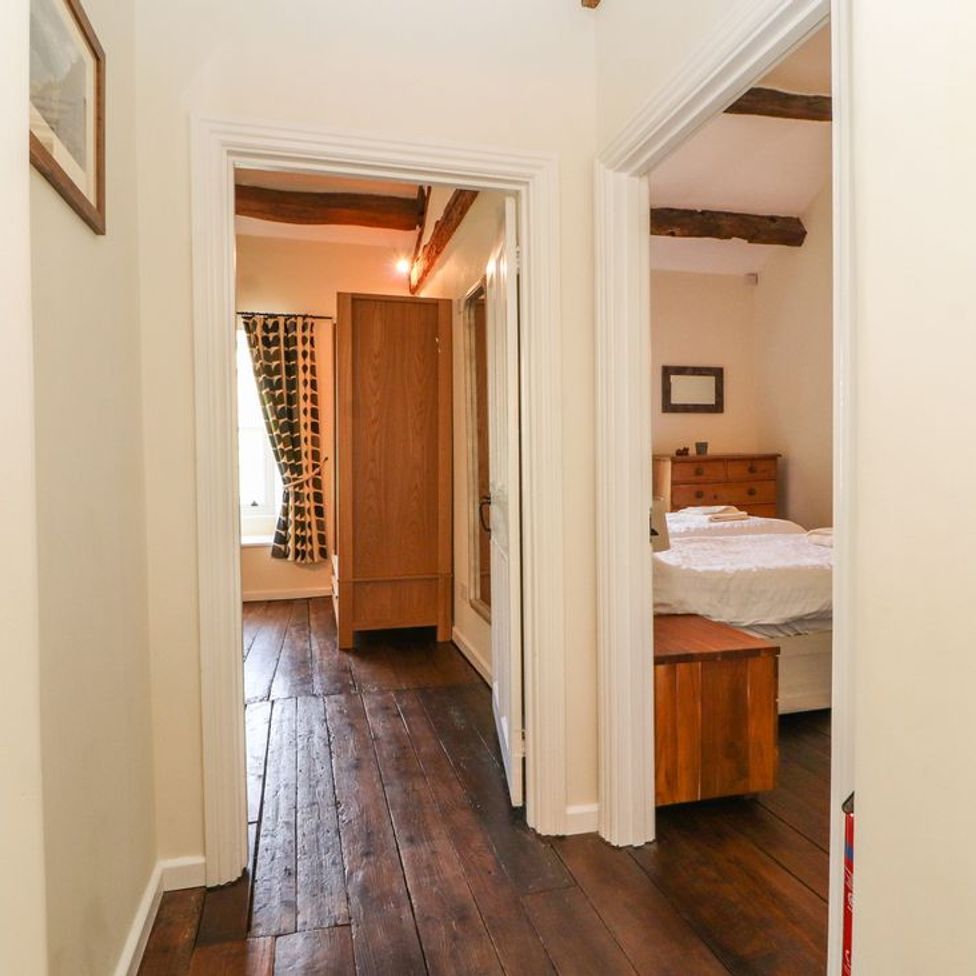 Hallway with wooden floor leading to a bedroom with bed and dresser and another room with wardrobe and window at Roger Pot in Garsdale near Sedbergh