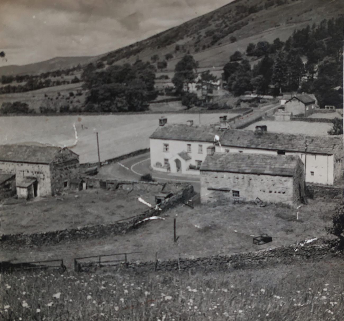 A historical photograph looking down over a Garsdale valley of stone farmhouses, barns and dry-stone walls