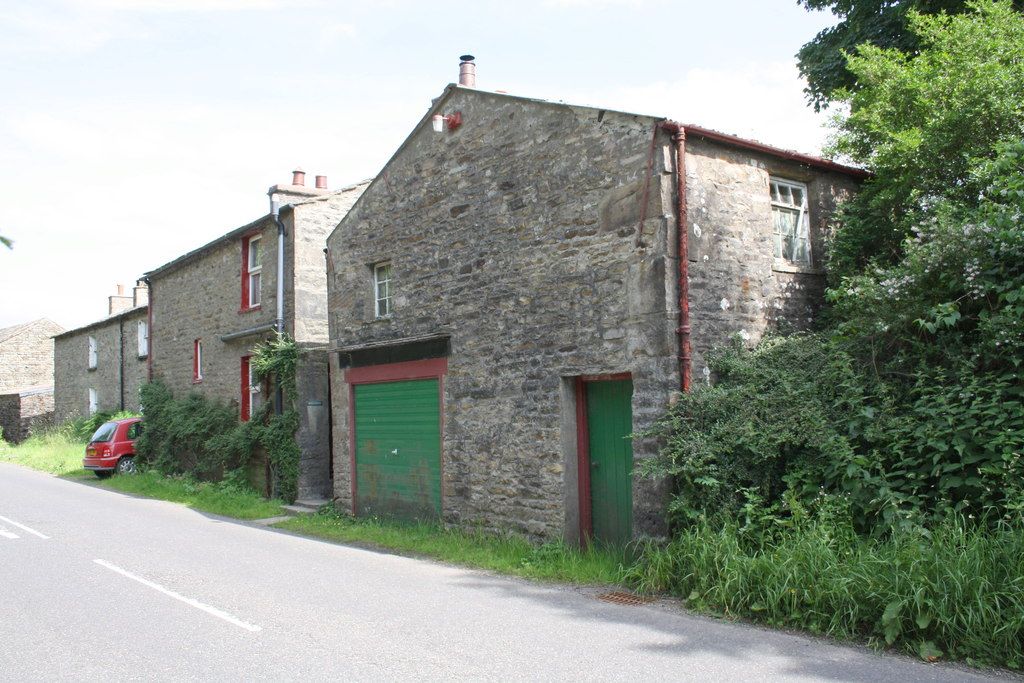 A row of old Garsdale stone houses with green and red painted doors beside a country road in summer