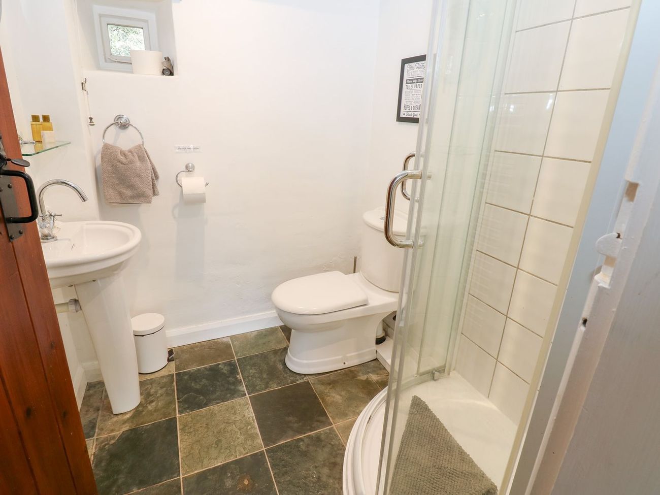 The ground floor shower room at Farrier's Cottage, with a corner shower cubicle, WC, pedestal basin and slate flagged floor