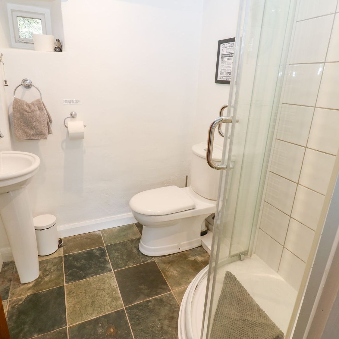 The ground floor shower room at Farrier's Cottage, with a corner shower cubicle, WC, pedestal basin and slate flagged floor