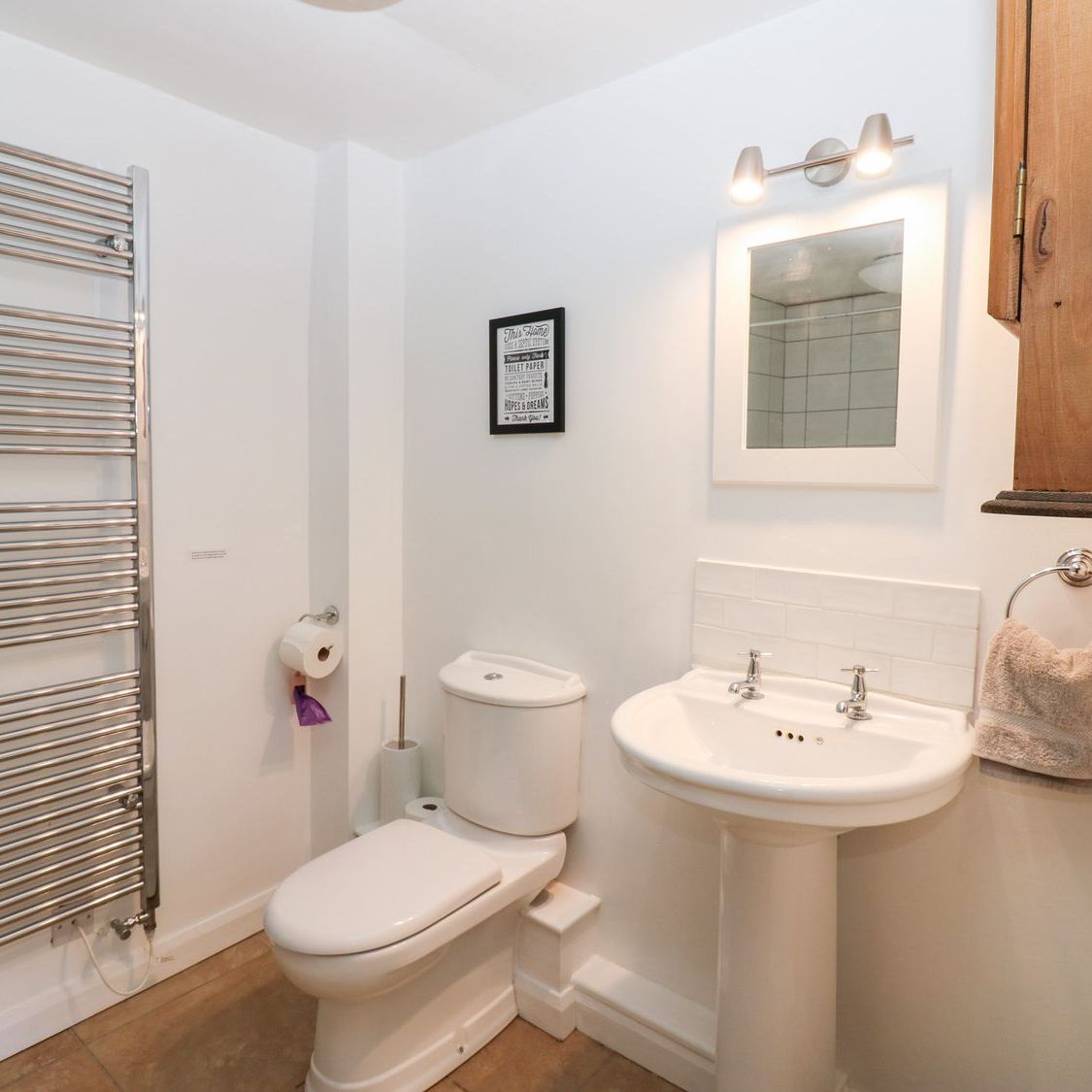 A view across the ground floor shower room at Farrier's Cottage, showing the heated towel rail, WC, pedestal basin and mirror