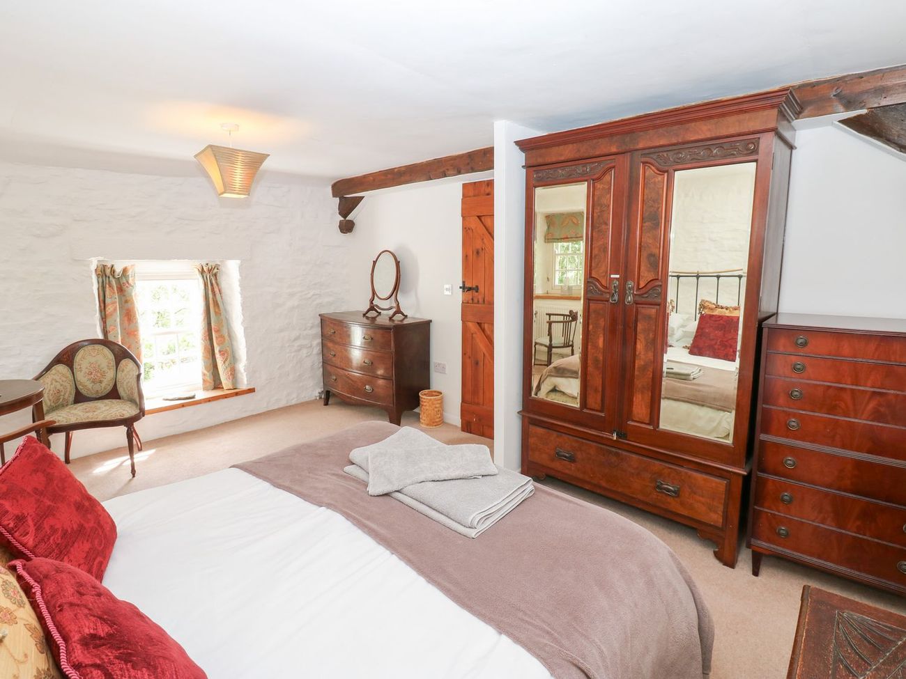 The king-size bedroom at Farrier's Cottage, with a mirrored mahogany wardrobe, chest of drawers and a deep window seat under a small cottage window