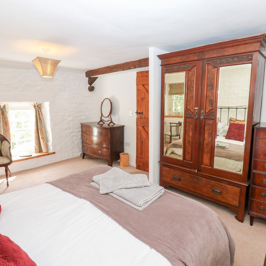 The king-size bedroom at Farrier's Cottage, with a mirrored mahogany wardrobe, chest of drawers and a deep window seat under a small cottage window