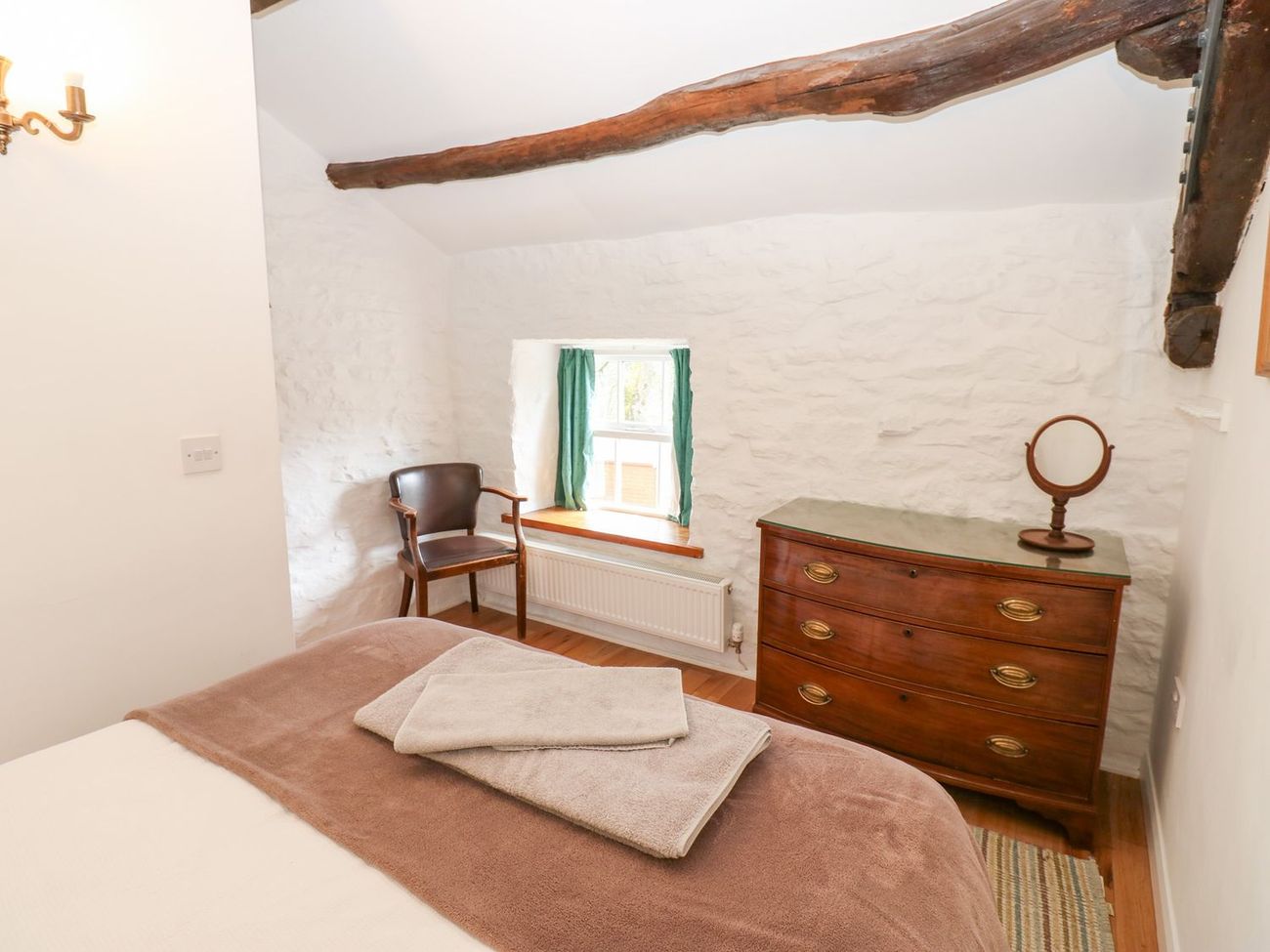A bedroom at Farrier's Cottage with an exposed roof beam overhead, an antique chest of drawers and towels laid out on the bed
