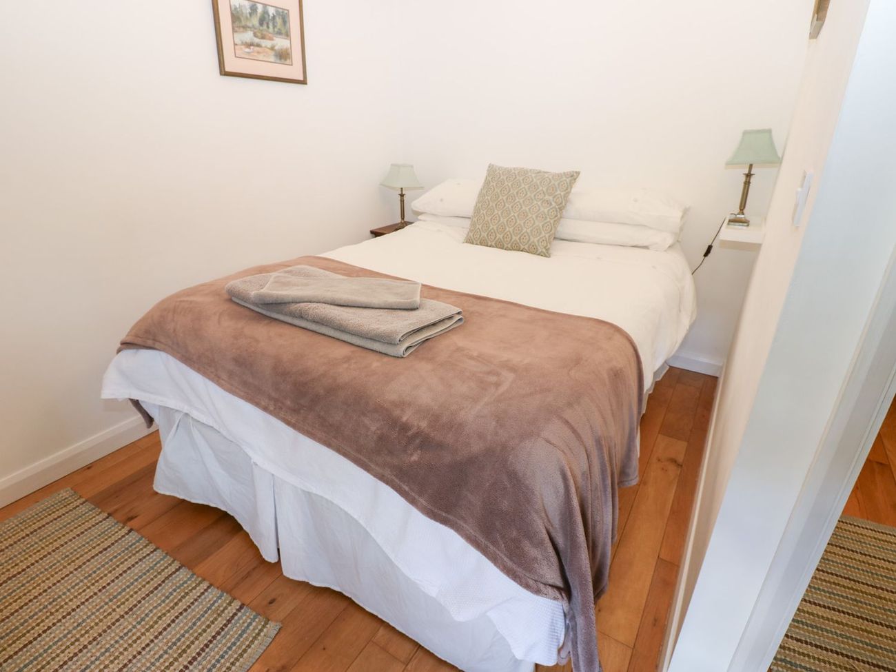 A double bedroom at Farrier's Cottage with a made-up bed, a pair of bedside lamps and a wooden floor with woven rugs