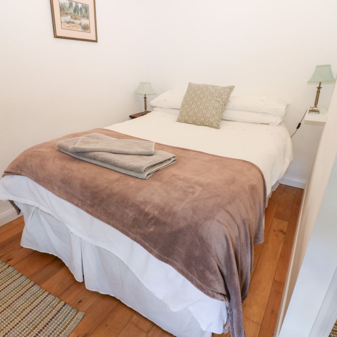 A double bedroom at Farrier's Cottage with a made-up bed, a pair of bedside lamps and a wooden floor with woven rugs