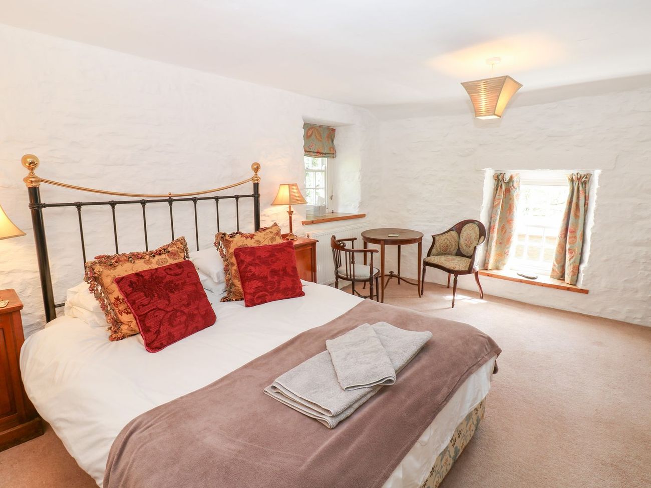 The king-size bedroom at Farrier's Cottage, with whitewashed stone walls, a small table and two antique chairs beside the window
