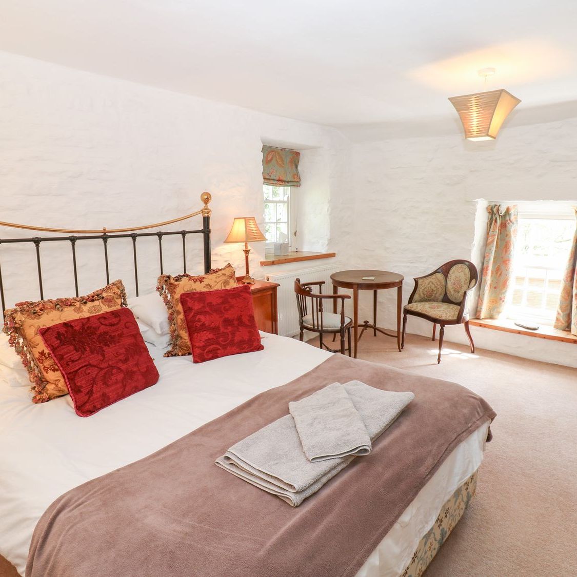 The king-size bedroom at Farrier's Cottage, with whitewashed stone walls, a small table and two antique chairs beside the window