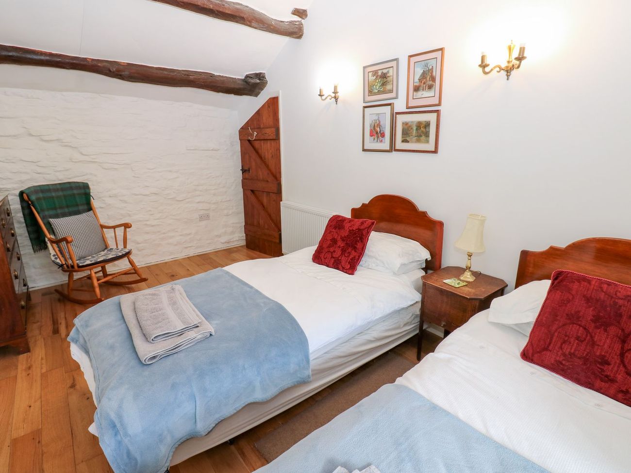 The twin bedroom at Farrier's Cottage, with two single beds, a rocking chair against the exposed stone wall and beams across the ceiling