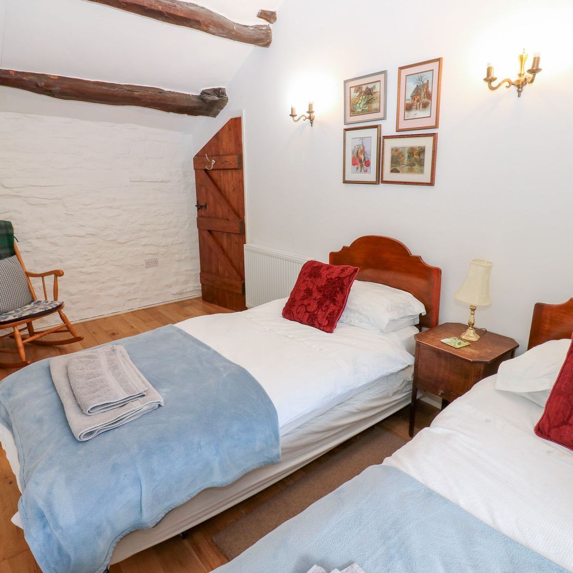The twin bedroom at Farrier's Cottage, with two single beds, a rocking chair against the exposed stone wall and beams across the ceiling