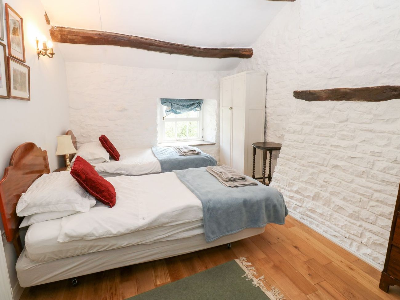 The twin bedroom at Farrier's Cottage, looking towards a deep-set window between whitewashed stone walls and roof beams