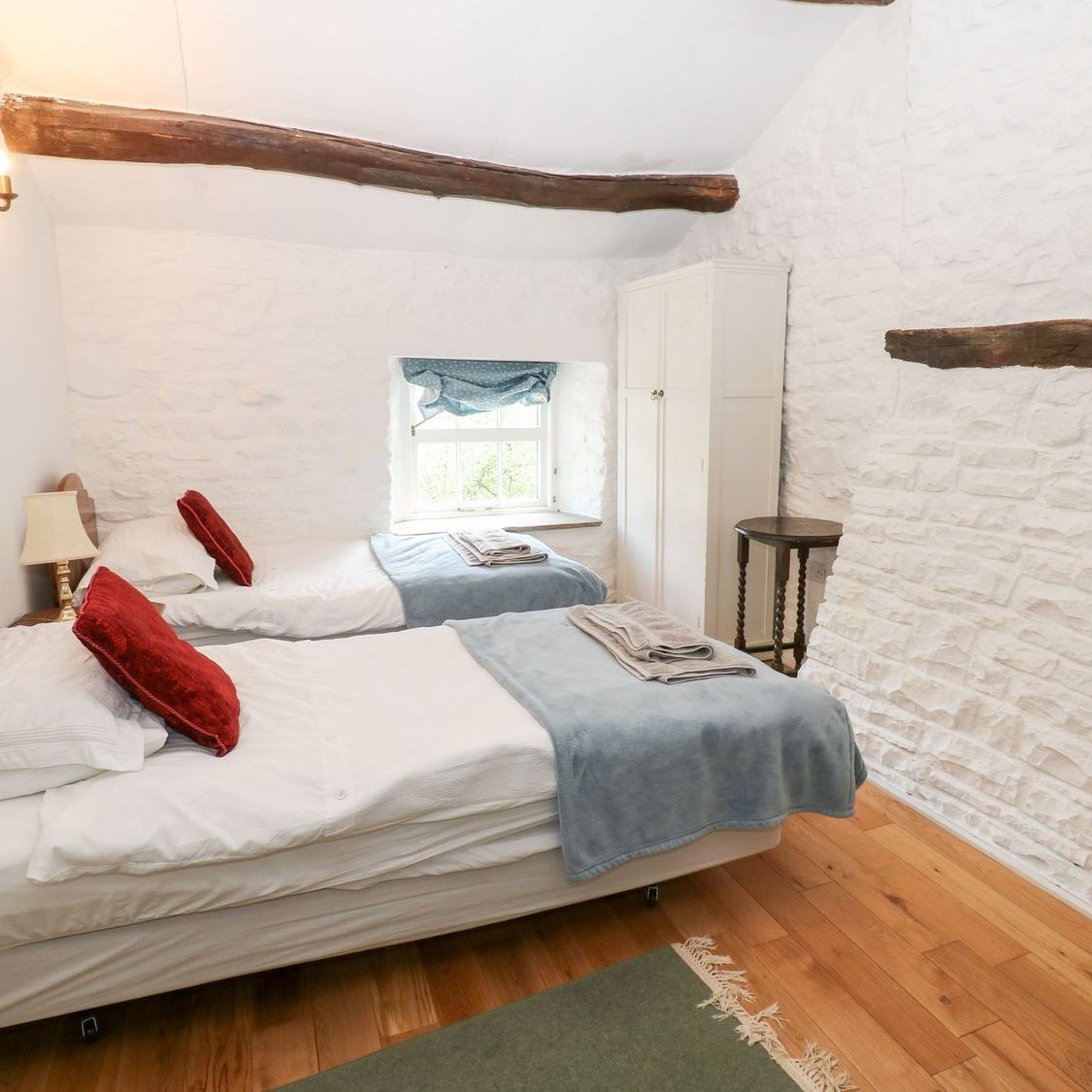 The twin bedroom at Farrier's Cottage, looking towards a deep-set window between whitewashed stone walls and roof beams