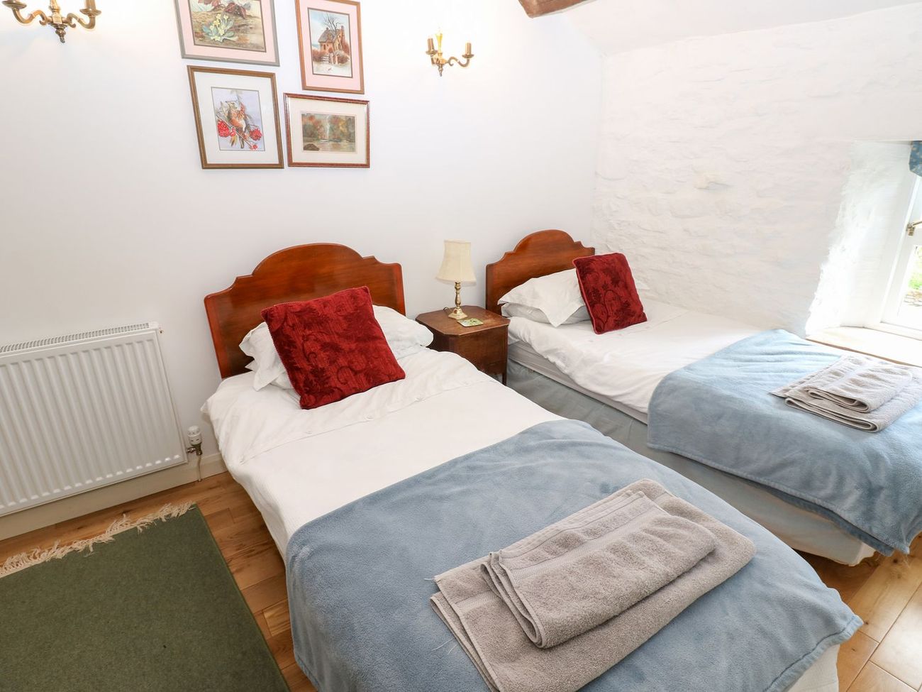 Two single beds made up with towels in the twin bedroom at Farrier's Cottage, with watercolours on the wall above
