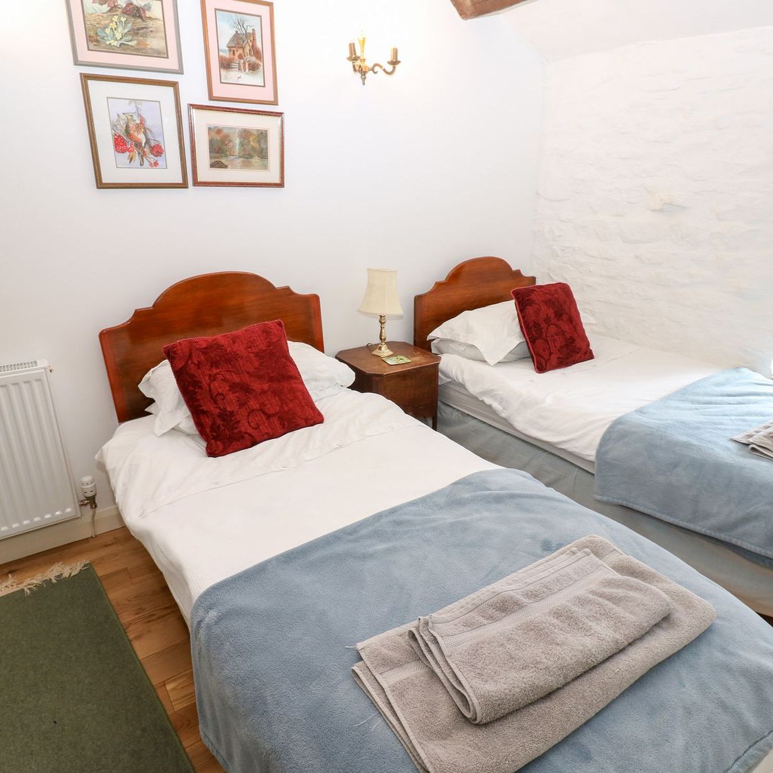 Two single beds made up with towels in the twin bedroom at Farrier's Cottage, with watercolours on the wall above