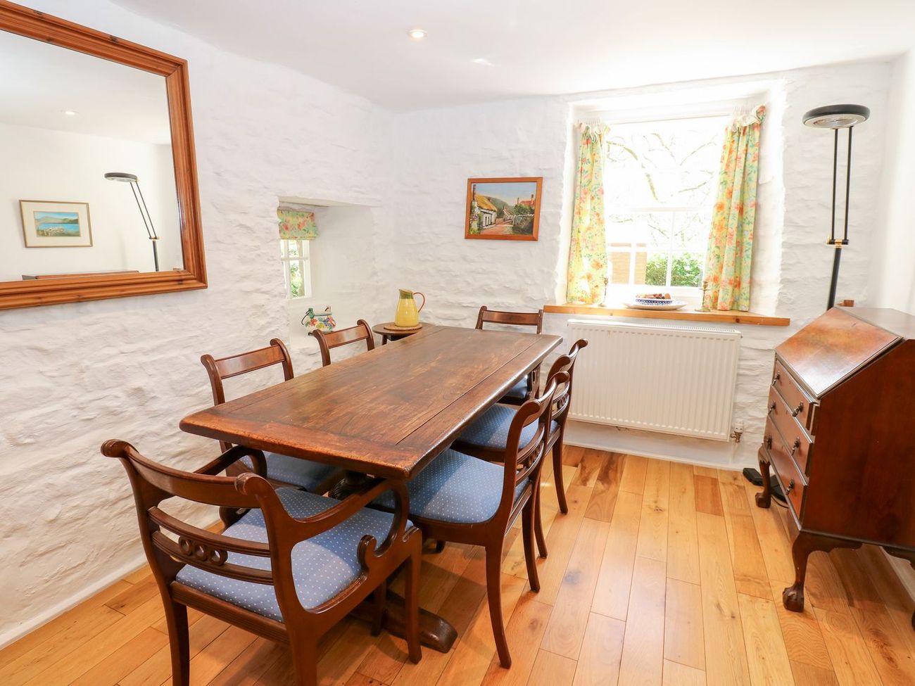 The dining room at Farrier's Cottage, with a long wooden table seating six, whitewashed stone walls and a window onto the garden