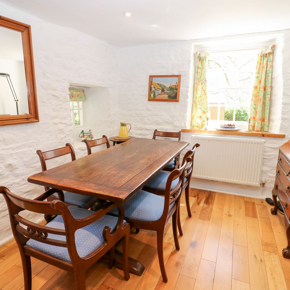 The dining room at Farrier's Cottage, with a long wooden table seating six, whitewashed stone walls and a window onto the garden