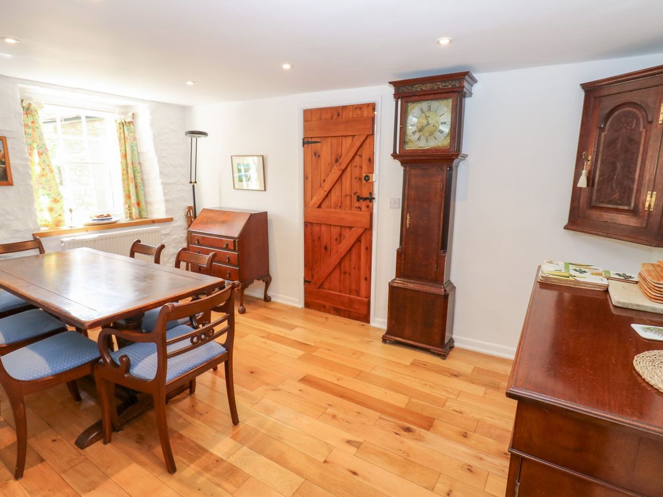 The dining room at Farrier's Cottage, with a longcase clock, a bureau and a plank door onto the hall