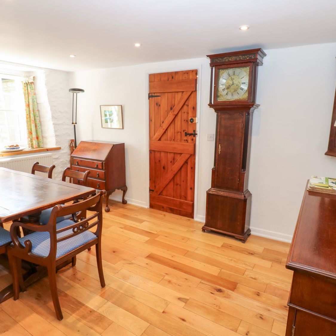 The dining room at Farrier's Cottage, with a longcase clock, a bureau and a plank door onto the hall