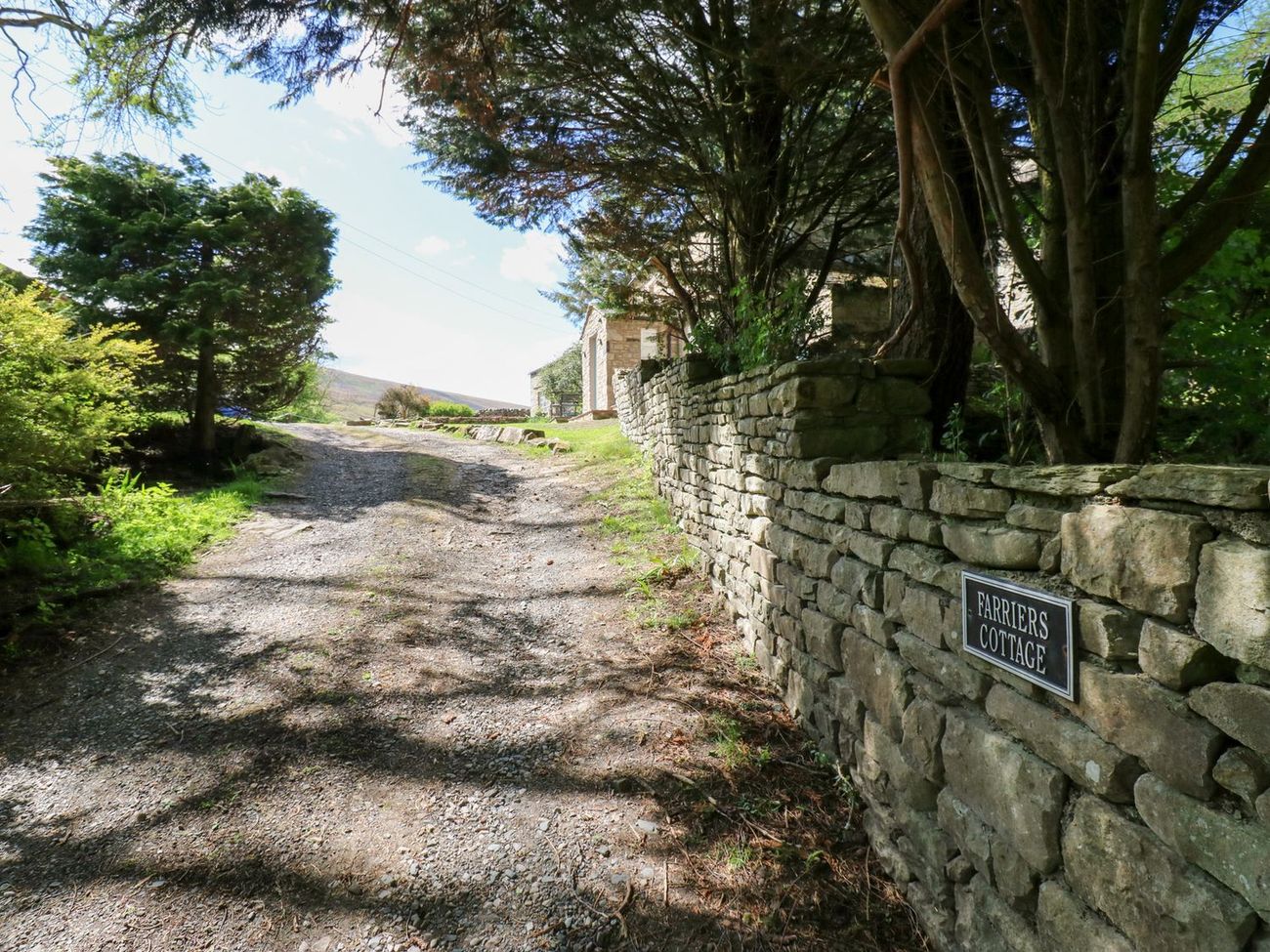 The gravel track up to Farrier's Cottage, with the nameplate set into the dry-stone wall and the fell rising beyond