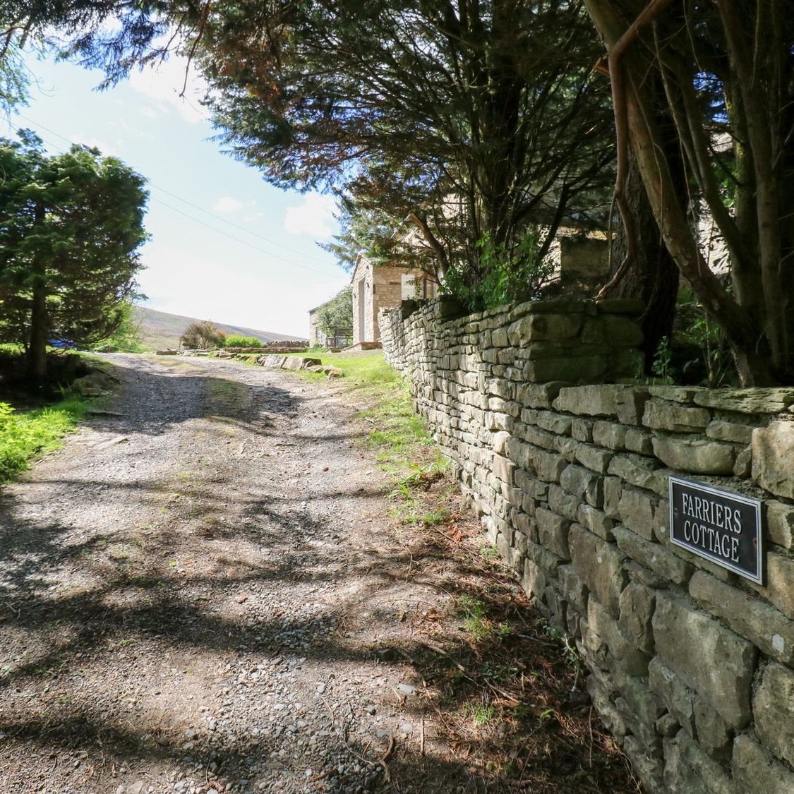 The gravel track up to Farrier's Cottage, with the nameplate set into the dry-stone wall and the fell rising beyond