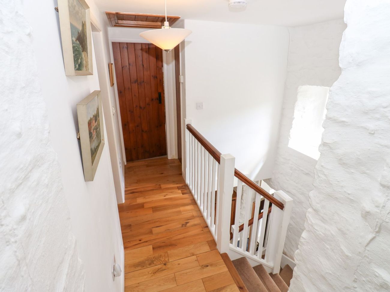 The first floor landing at Farrier's Cottage, with paintings on the whitewashed walls and the stairs dropping away to the right