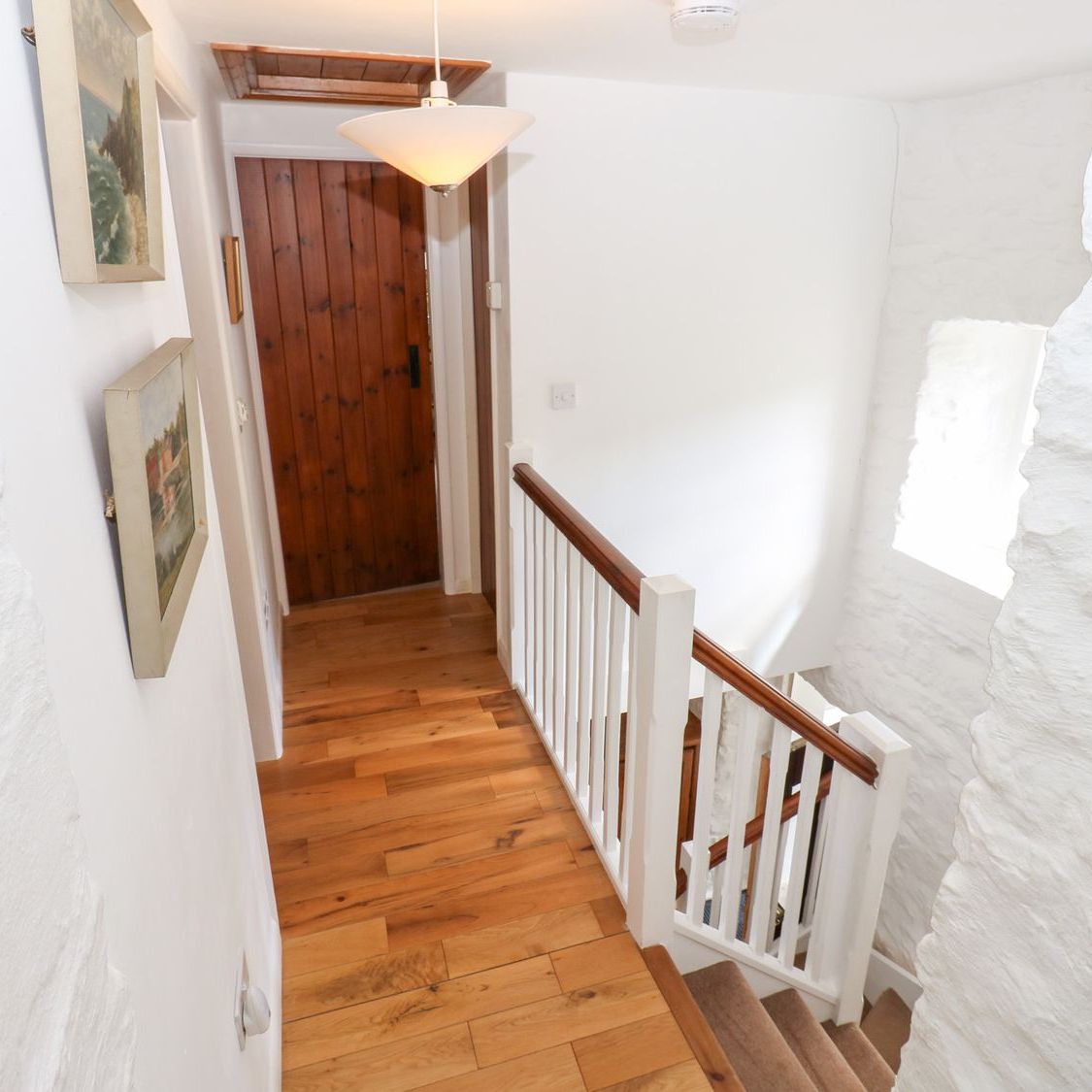 The first floor landing at Farrier's Cottage, with paintings on the whitewashed walls and the stairs dropping away to the right