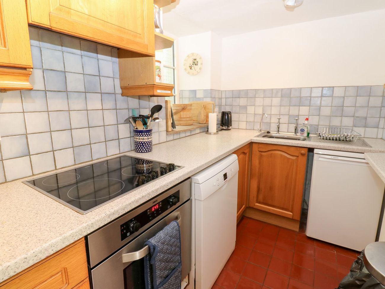 The kitchen at Farrier's Cottage, with an electric hob and oven, dishwasher, sink and a quarry tiled floor