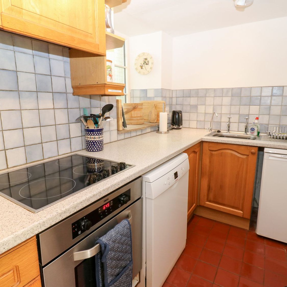 The kitchen at Farrier's Cottage, with an electric hob and oven, dishwasher, sink and a quarry tiled floor