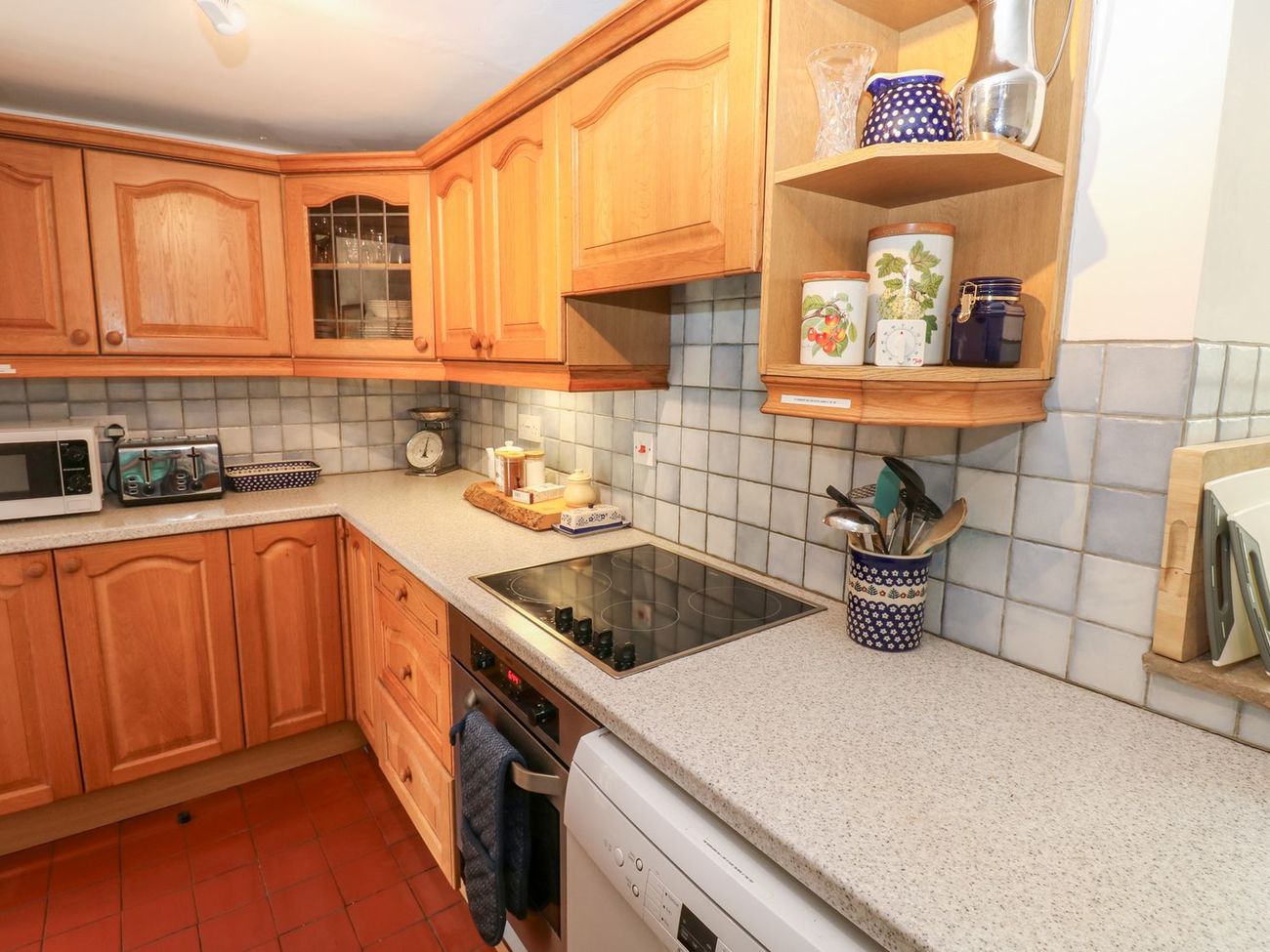 The kitchen at Farrier's Cottage, with oak units, a tiled splashback and shelves of storage jars