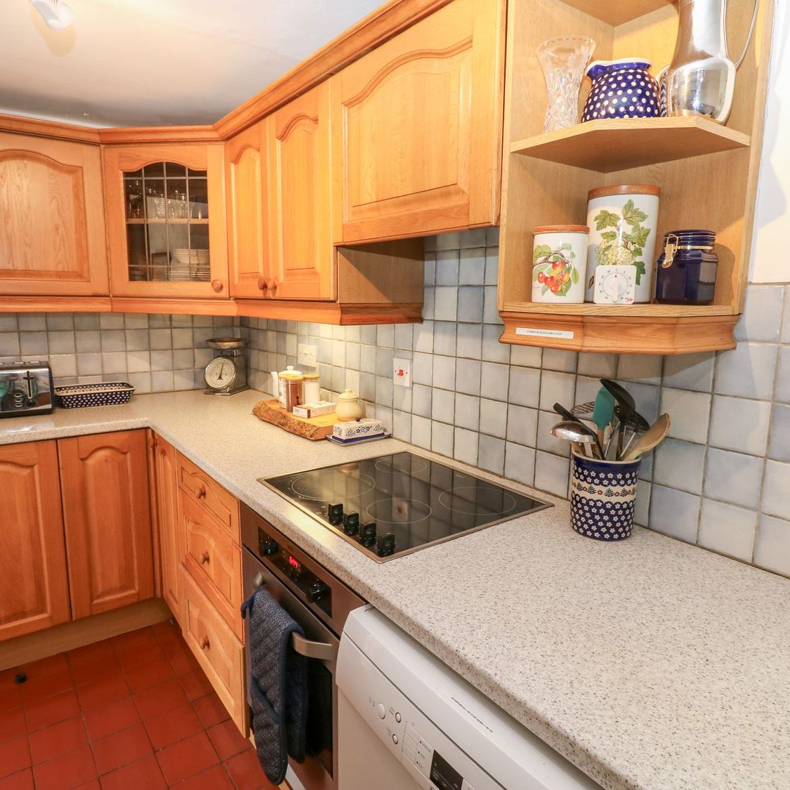 The kitchen at Farrier's Cottage, with oak units, a tiled splashback and shelves of storage jars