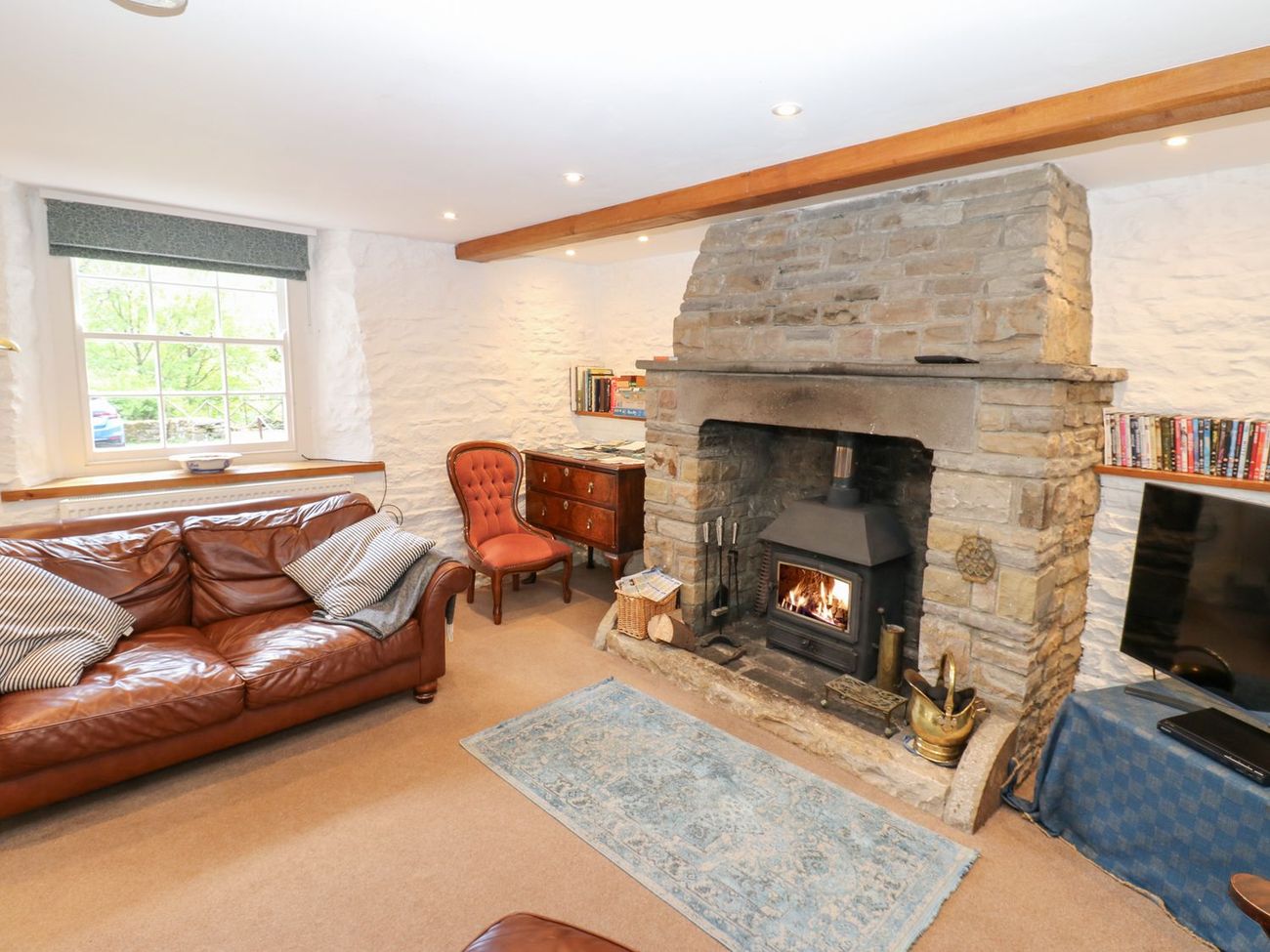The sitting room at Farrier's Cottage, with a woodburning stove lit in the stone fireplace and a leather sofa beside the window