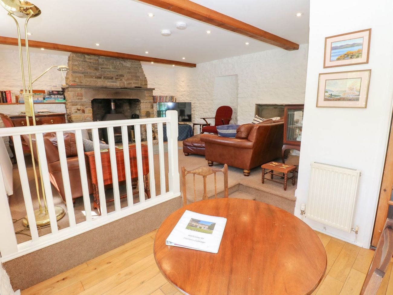 Looking from the dining table into the sitting room at Farrier's Cottage, with leather sofas gathered around the stone fireplace
