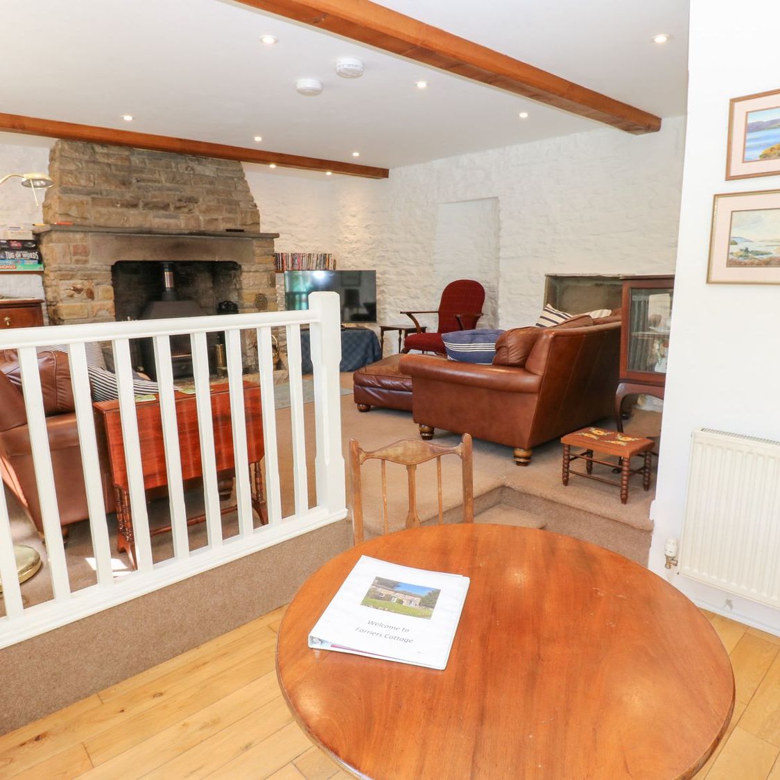 Looking from the dining table into the sitting room at Farrier's Cottage, with leather sofas gathered around the stone fireplace