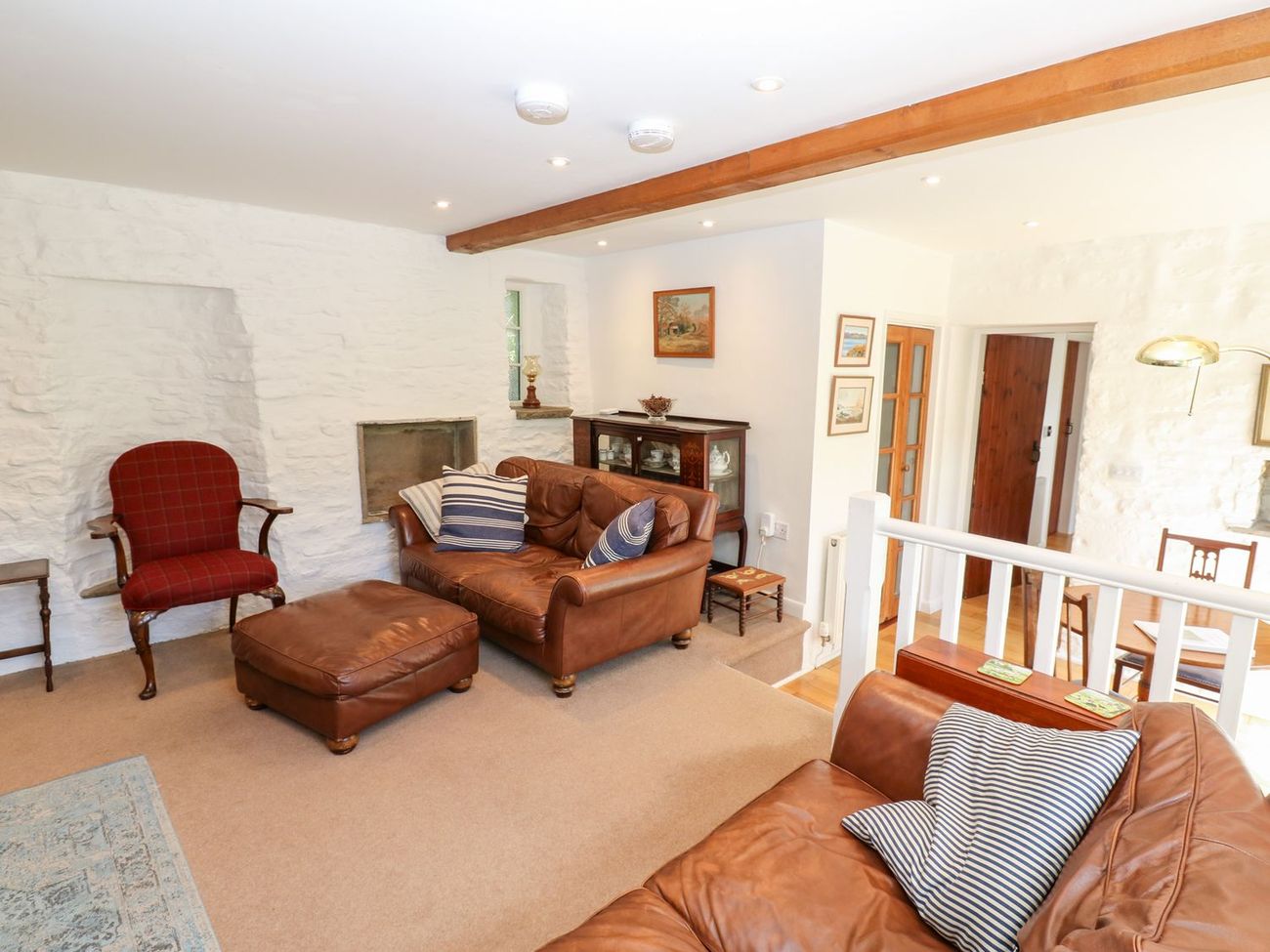 The sitting room at Farrier's Cottage, with leather sofas, a footstool and a tartan armchair against the whitewashed stone wall