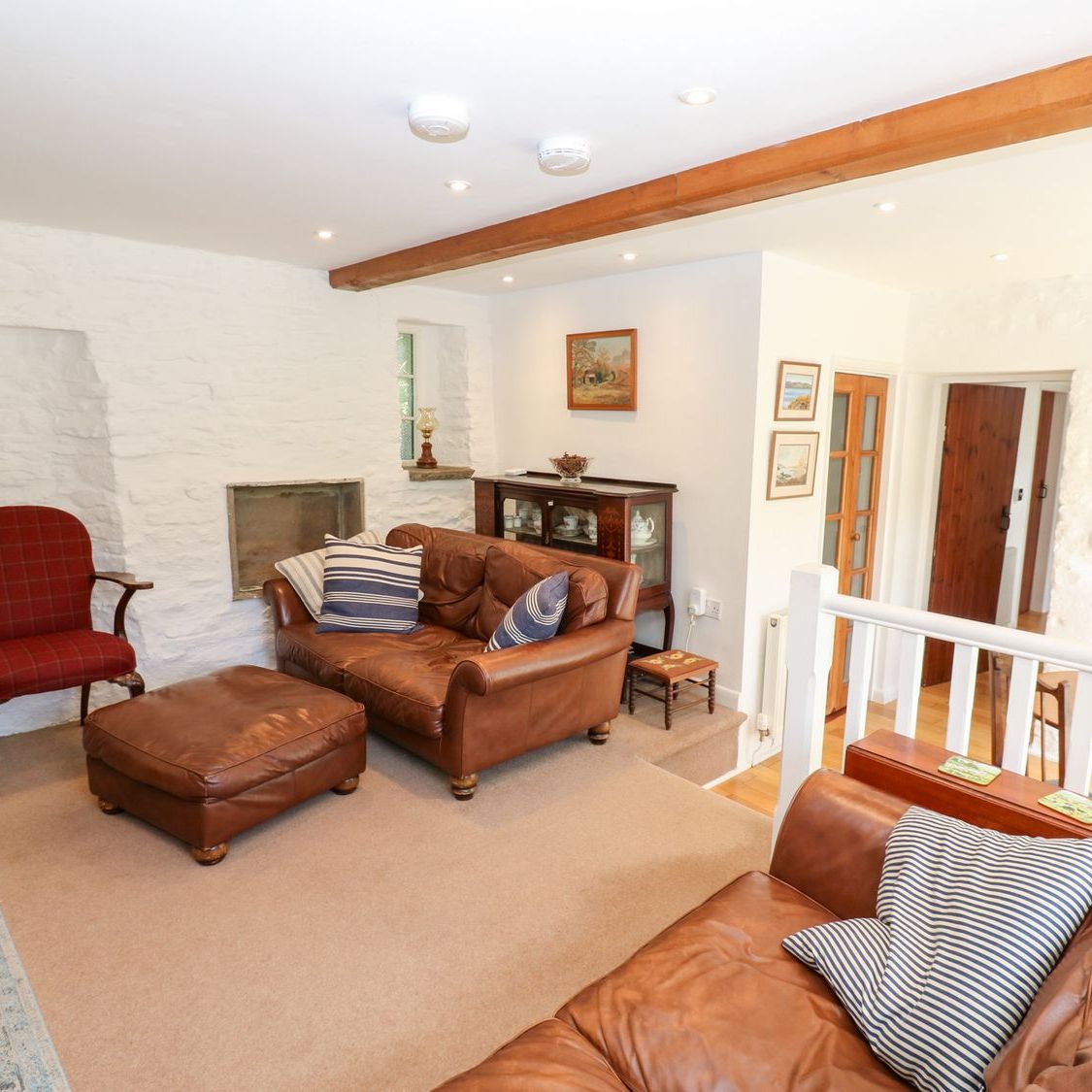 The sitting room at Farrier's Cottage, with leather sofas, a footstool and a tartan armchair against the whitewashed stone wall