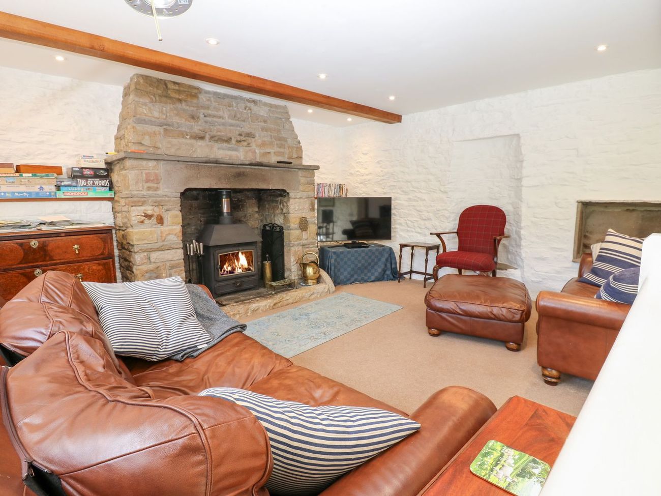 The sitting room at Farrier's Cottage, with the woodburning stove alight, board games on the shelf and leather sofas facing the fire