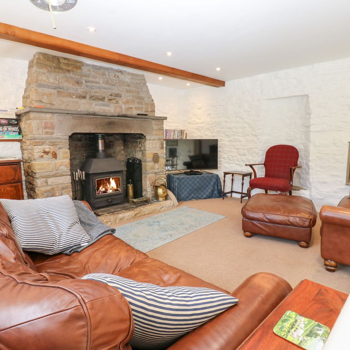 The sitting room at Farrier's Cottage, with the woodburning stove alight, board games on the shelf and leather sofas facing the fire