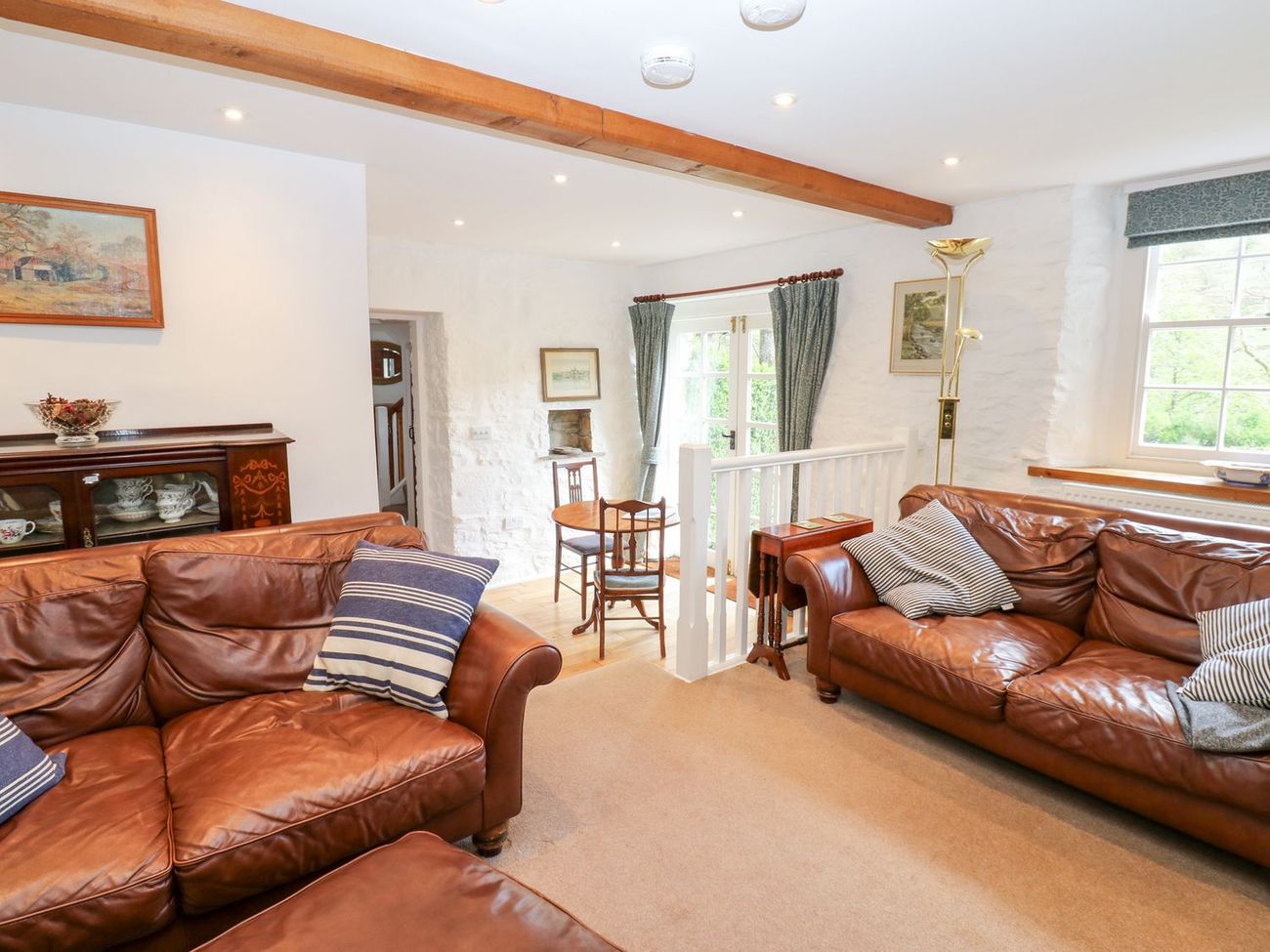 The sitting room at Farrier's Cottage, with two leather sofas, a glazed dresser and French doors onto the garden