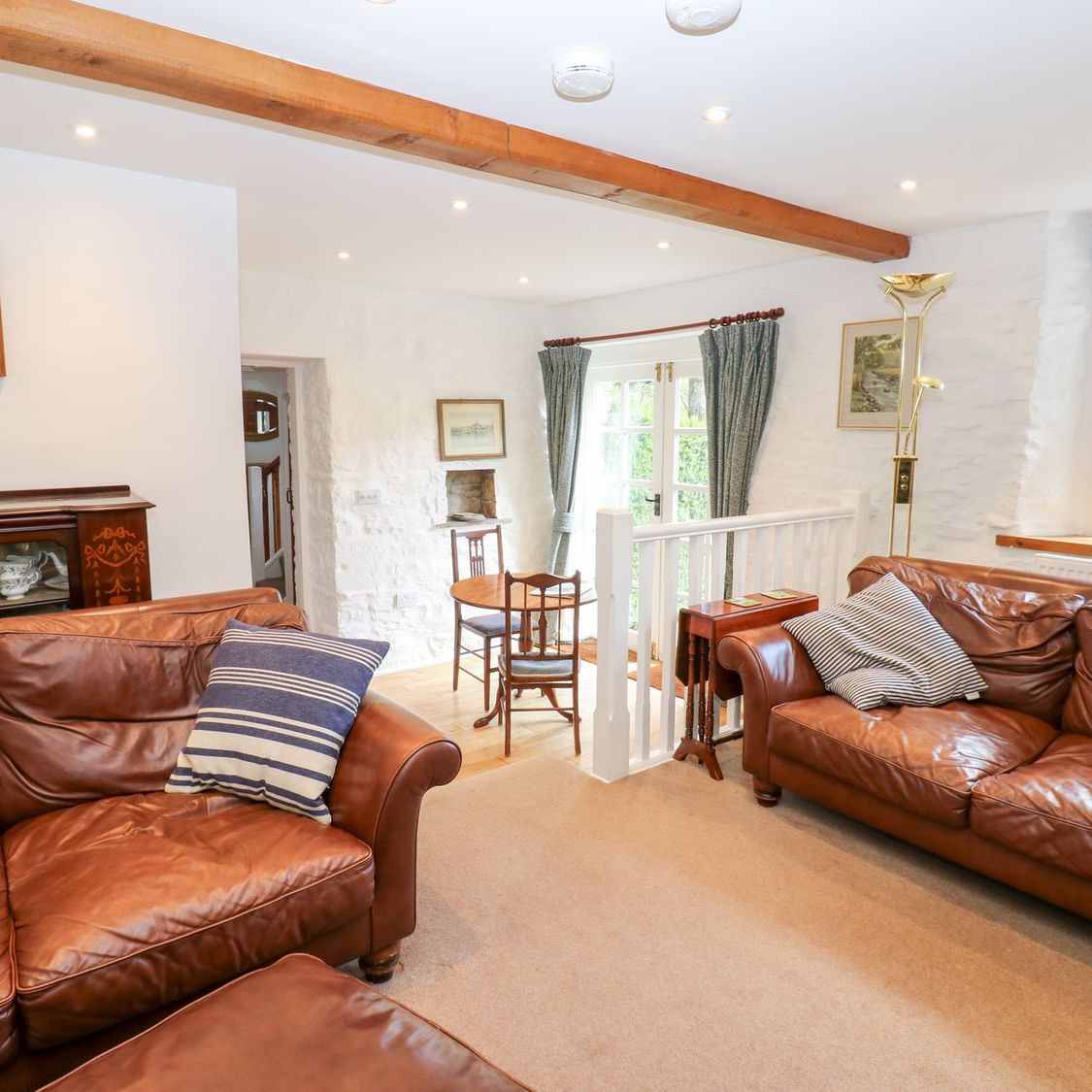 The sitting room at Farrier's Cottage, with two leather sofas, a glazed dresser and French doors onto the garden
