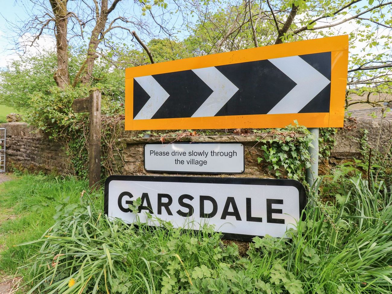 The Garsdale village sign beside the road, with a request to drive slowly through the village