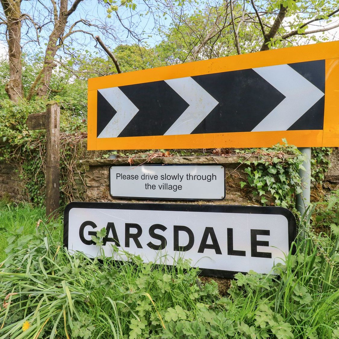 The Garsdale village sign beside the road, with a request to drive slowly through the village